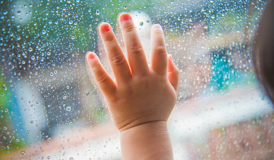 Mano de bebé sobre la ventanilla con lluvia del coche